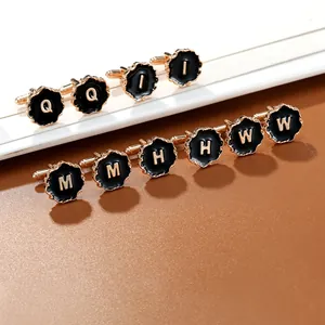 Detailed close-up of golden alphabet cufflinks with black enamel on a brown surface