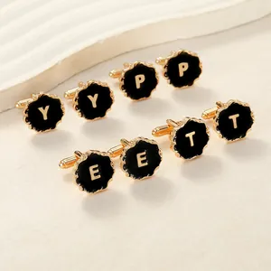 Close-up of gold petal-edged cufflinks with black enamel and custom gold letters