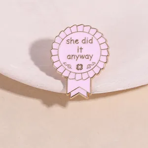 Detail view of pink enamel medal brooch with black 'she did it anyway' text and gold edging