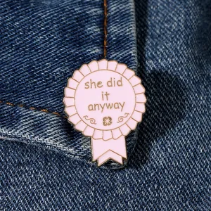 Pink enamel badge with 'she did it anyway' text pinned on denim jacket