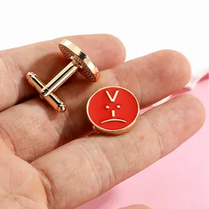 Close-up of gold-plated round cufflinks with red enamel angry face on palm