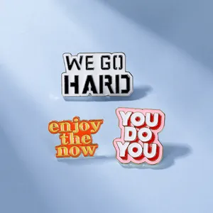 Dettaglio di spille in smalto con citazioni WE GO HARD e YOU DO YOU su sfondo azzurro