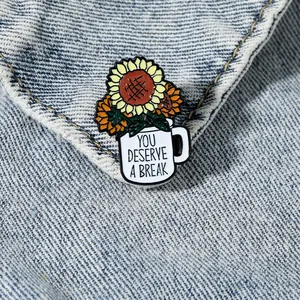 Enamel sunflower pin in a coffee cup on denim background with 'You deserve a break' text