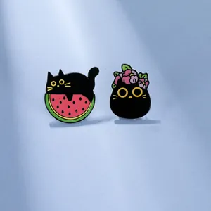 Dettaglio di spille in smalto gatto nero su anguria con decorazione floreale rosa