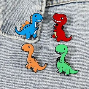 Lot de quatre broches dinosaures de dessin animé en émail sur un fond en jean bleu