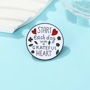 Détail d'une broche ronde en émail avec citation Grateful Heart et fleurs