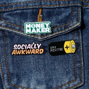 Close-up of three colorful enamel pins including Money Maker and Stay Positive on denim jacket