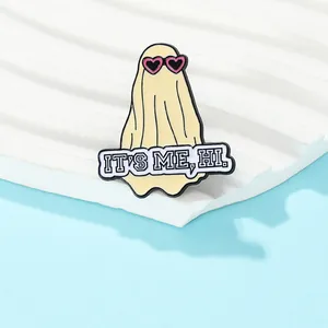 Close-up of yellow ghost enamel pin with pink heart sunglasses and 'IT'S ME, HI' text