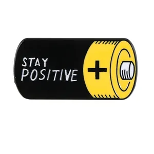 Battery shaped metal enamel pin featuring STAY POSITIVE text and yellow plus sign