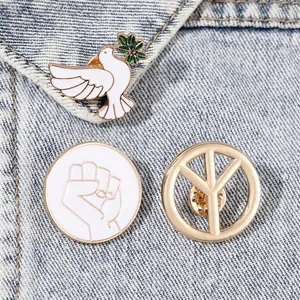 Three enamel pins featuring a white peace dove and gold symbol on blue denim fabric