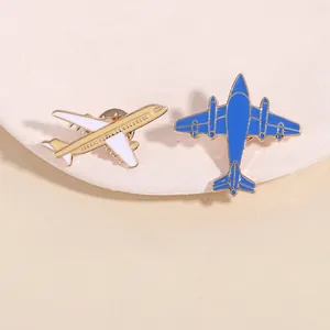 Vue détaillée de mini broches avion en or et bleu posées sur un plateau en pierre blanche