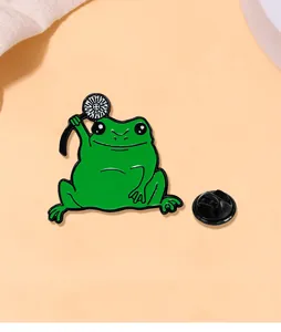 Détail d'une épingle émaillée grenouille verte avec pissenlit sur un fond rose doux