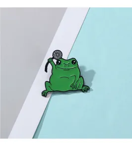 Détail d'une épingle en émail grenouille verte tenant une fleur sur fond tricolore pastel