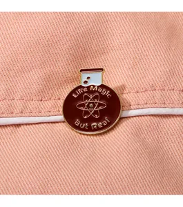 Primer plano de un pin esmaltado redondo con símbolo atómico en tela rosa