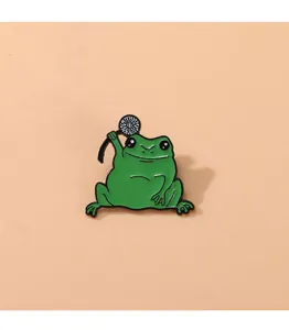 Détail d'une broche grenouille en émail vert tenant une fleur blanche aux contours noirs