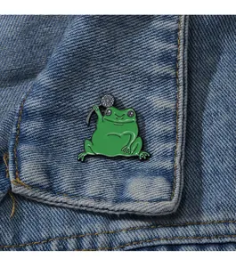 Épingle en émail avec un crapaud vert tenant une fleur sur la poche d'une veste en jean