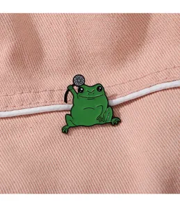 Détail d'un pin's émaillé grenouille verte sur un tissu en denim rose texturé