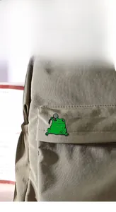 Détail d'un pin's en émail de grenouille verte attaché à un sac à dos en toile marron