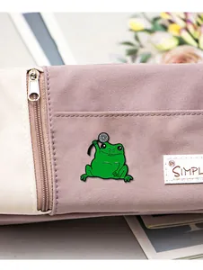 Détail du pin's grenouille en émail vert avec fleur blanche sur un sac en toile mauve
