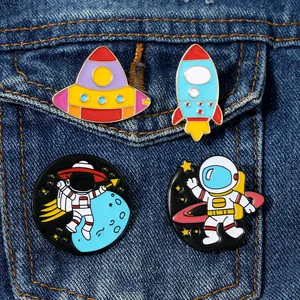 Close-up of four creative astronaut enamel pins attached to a blue denim jacket pocket