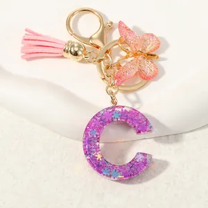 Dettaglio portachiavi lettera C in resina viola con glitter, farfalla rosa e nappa rosa