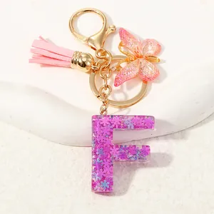 Dettaglio portachiavi lettera F in resina viola con glitter, farfalla e nappa rosa