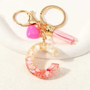 Detail of resin letter C keychain with pink tassels and gold flakes on white ceramic