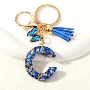 Detail of blue resin letter C keychain with gold foil, blue tassel and butterfly charm