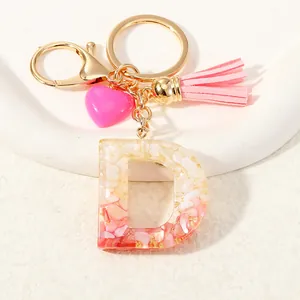 Detailed view of pink resin letter D keychain with gold foil, tassel and heart charm