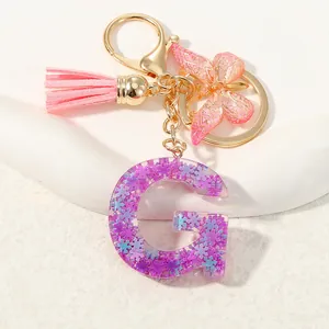 Dettaglio portachiavi lettera G in resina viola con paillettes, nappa e farfalla rosa