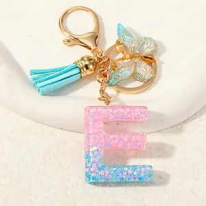 Close-up of glitter resin letter E keychain with blue tassel and gold butterfly