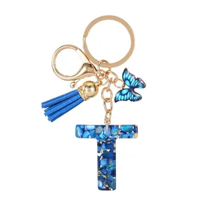 Blue resin letter T keychain with gold foil, tassel and butterfly charm on white background