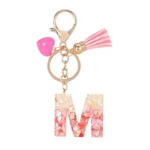 Pink resin letter M keychain with gold flakes, tassel, and heart charm on white background
