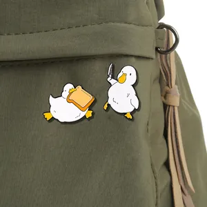 Cute enamel duck pins with toast and knife designs pinned on a green canvas backpack