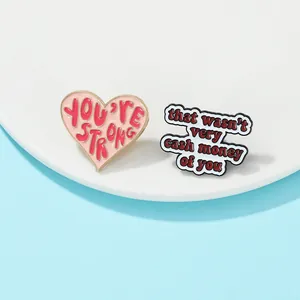 Detail of two enamel pins with You're Strong and cash money text on a blue background