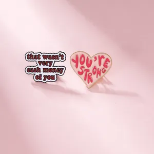 Detail of enamel cloud and heart pins with motivational text on pink backdrop
