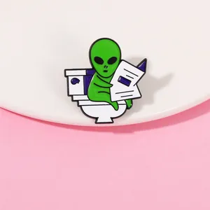 Détail de l'épingle en émail d'un extraterrestre sur les toilettes lisant un journal