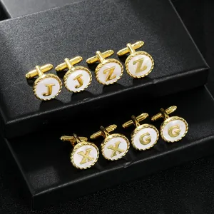 Macro detail of gold-plated alphabet cufflinks with white shell inlay on black display