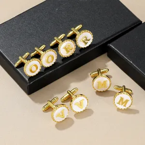 Golden round cufflinks with white shell inlay and alphabet letters on black jewelry box