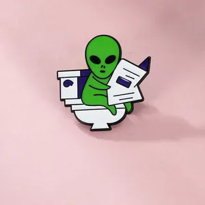 Broche en émail humoristique d'un extraterrestre vert lisant sur des toilettes