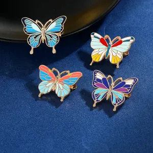 Détail de quatre broches papillon colorées avec bords en métal doré sur un tissu bleu foncé