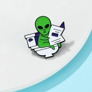 Épingle en émail humoristique d'un extraterrestre vert lisant sur des toilettes