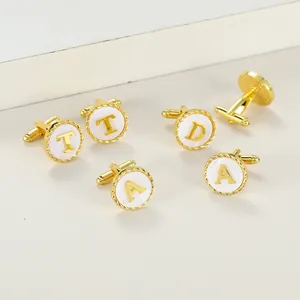 Detail of gold cufflinks featuring white circular alphabet initials and braided borders