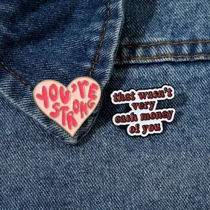 Detail of pink heart and white text enamel pins on a dark blue denim jacket collar