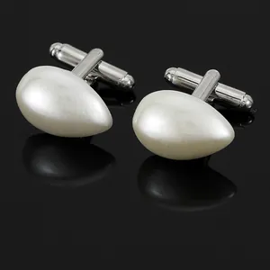 Détail de boutons de manchette argentés avec perles gouttes sur fond noir brillant