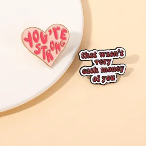 Detailed close-up of enamel pins with 'YOU'RE STRONG' heart and viral slogan text