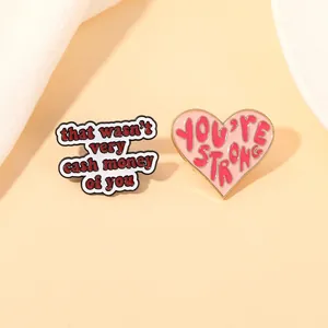 Detail shot of enamel brooches featuring That wasn't very cash money of you and You're strong