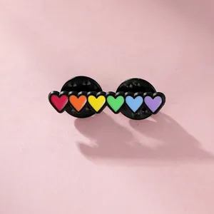 Detail of rainbow heart enamel pin featuring black metal base and double butterfly clutches
