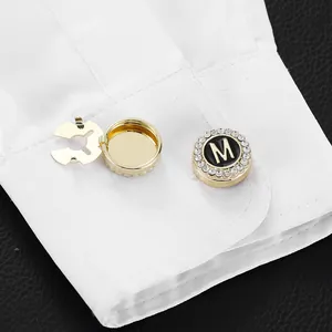 Gold-plated letter M cufflinks with black enamel and rhinestones on a white shirt sleeve