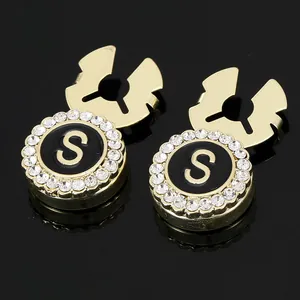 Macro view of gold plated cufflinks with black enamel letter S and white zircon border